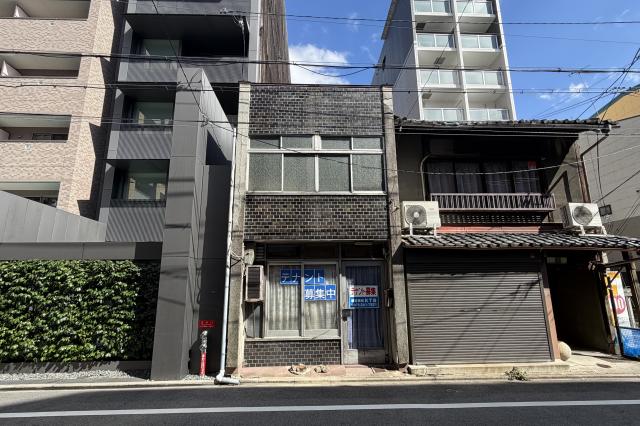中京区壺屋町の貸店舗の正面外観。濃い色のタイル張りの2階建てで、2階に横長の窓、1階にテナント募集の貼り紙がある窓と入口ドアが並ぶ