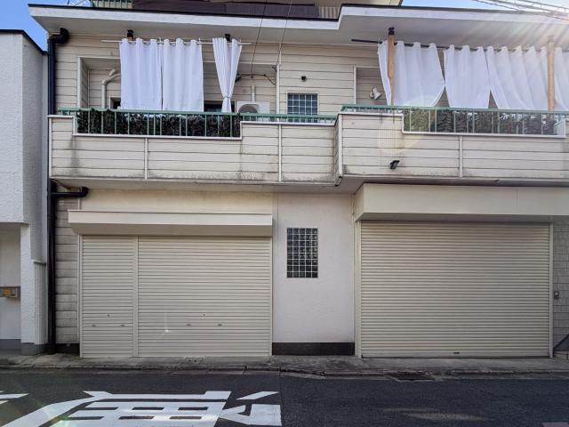 新桝屋町店舗の正面外観。1階は左に庇付きの2連シャッター、中央にガラスブロック窓、右に大きなシャッターが並び、2階に緑の手すりのバルコニーがある