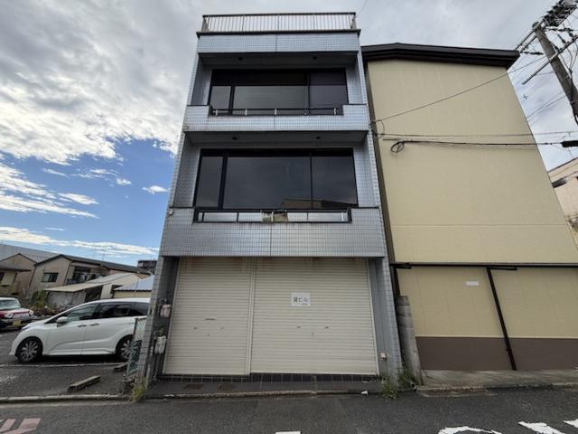 西院北矢掛町の3階建店舗付き住宅の正面外観。タイル張りの外壁、1階のシャッター、2階と3階の大きな窓、屋上の手すりが見える