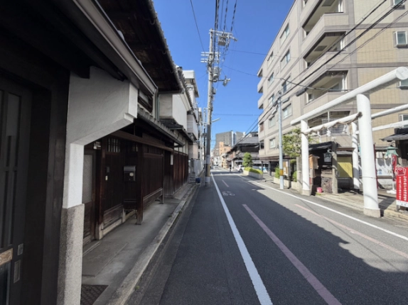 町家の軒先から見た周辺の街並み。向かい側に白い鳥居と中高層の建物が見える