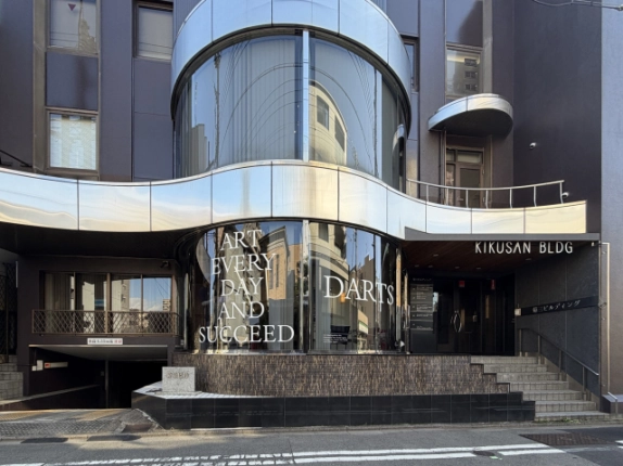 中京区の菊三ビル正面外観。曲線を描くステンレスの庇と円筒形のガラス窓が特徴で、右手に階段付きのエントランス、左手に地下駐車場の入口がある
