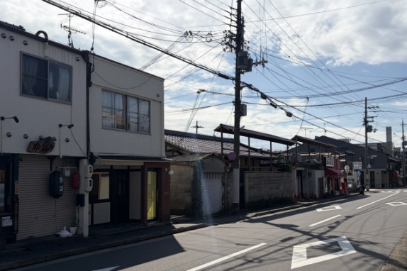 京都市北区の店舗前の通りを見通した街並み。左手に白い建物の1階店舗、道路沿いに瓦屋根の家屋やブロック塀が続く