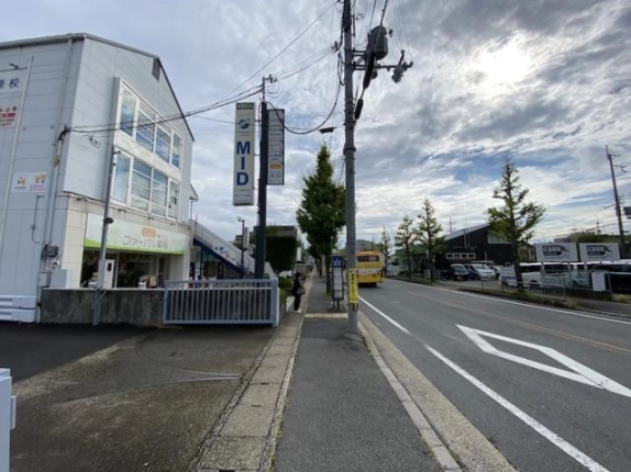 山陰街道の歩道から見た日章ビルと前面道路。左に建物と縦型看板、歩道沿いに電柱とバス停