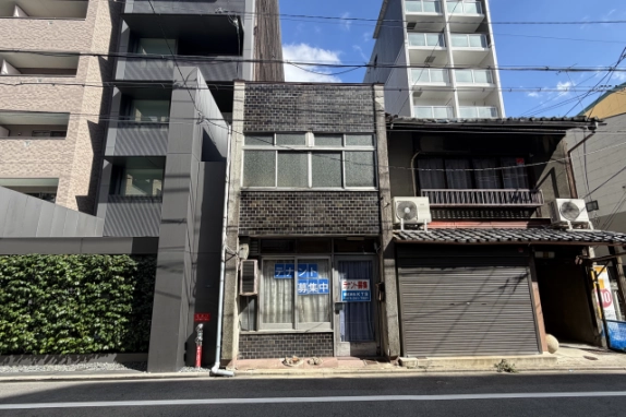 中京区壺屋町の貸店舗の正面外観。濃い色のタイル張りの2階建てで、2階に横長の窓、1階にテナント募集の貼り紙がある窓と入口ドアが並ぶ