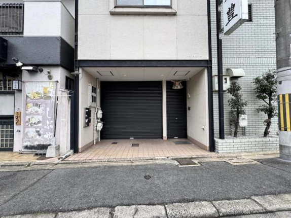 1階区画の正面。大小2枚の黒いシャッターが並び、手前はベージュのタイル床、左の壁にメーターボックスがある