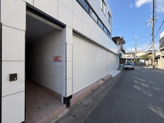 建物を左手に見た前面道路の反対方向。手前にタイル張りの入口、奥に交差点