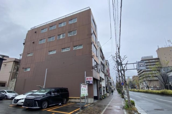 渡辺ビルの側面外観。茶色の外壁に並ぶ窓と隣接するコインパーキング