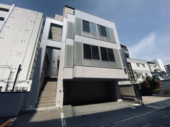 高辻室町の一棟貸事務所ビルを左斜め前から見上げた外観。正面左側に上階へ続くタイル張りの階段入口、右側に1階のシャッター付き車庫がある