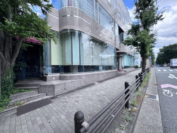 建物1階の曲面ガラスと正面沿いの歩道。左端には階段のある出入口