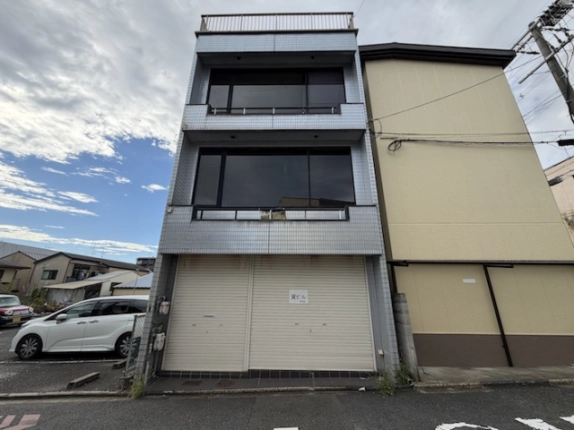 西院北矢掛町の3階建店舗付き住宅の正面外観。タイル張りの外壁、1階のシャッター、2階と3階の大きな窓、屋上の手すりが見える