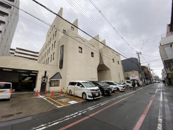 右斜め前から道路の先まで入れて写した外観。手前に赤いカラーコーンのある駐車区画、左端に屋内駐車場の入口が見える