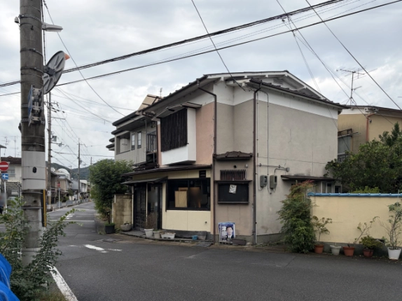 右斜め前から見た外観。グレーの側面外壁と右隣のクリーム色の塀、左手前にカーブミラー付きの電柱