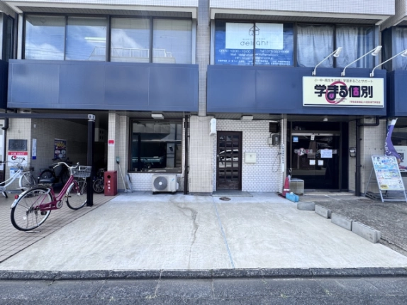 三輝ビル1F-Nの正面外観。店舗前の舗装スペースと青い帯状の外壁
