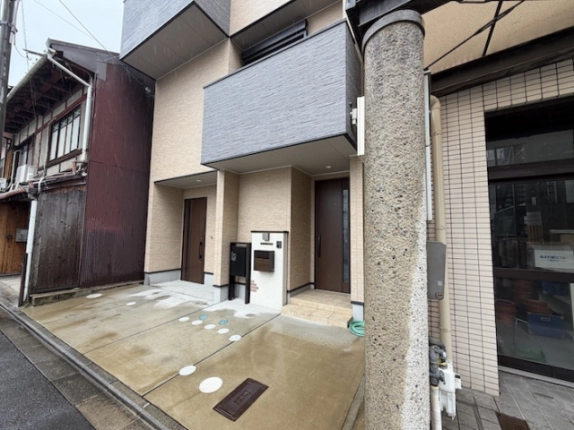1階貸店舗がある建物の入口まわり。茶色の扉と郵便受け、道路に面した舗装スペース
