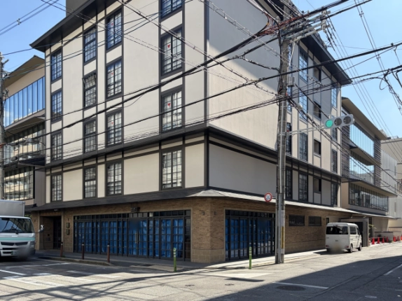 交差点の角から見たキオリエグゼ室町の全景。レンガ調の1階は通りに面した2面にガラス戸が並び、白壁と格子窓の上階、右手前に信号機と電柱が立つ