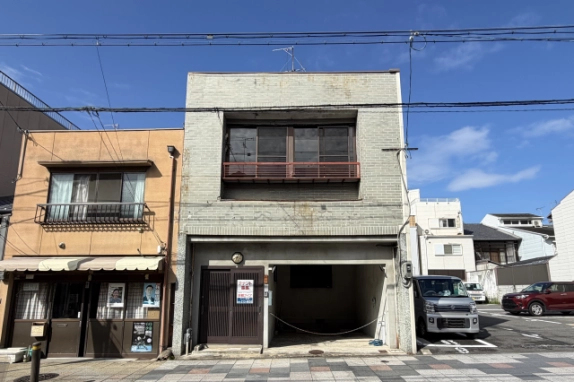 紫野下門前町の通りに面した2階建て店舗の正面外観。2階に赤茶の手すり付き窓、1階左に茶色の格子戸、右に車庫の開口部