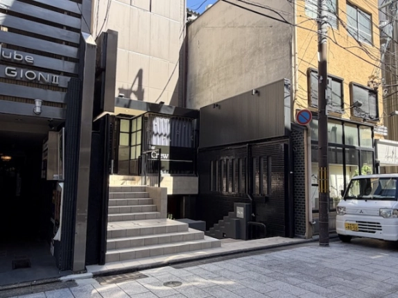 入口へ上がるタイル張りの階段と、1階の「Bar Crew」の看板を正面から見た様子。右側には黒いタイル張りの外壁が続く