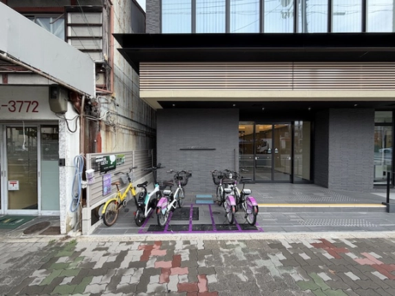 A号室の募集がある建物の1階正面。ガラス張りの出入口と歩道沿いの駐輪スペース