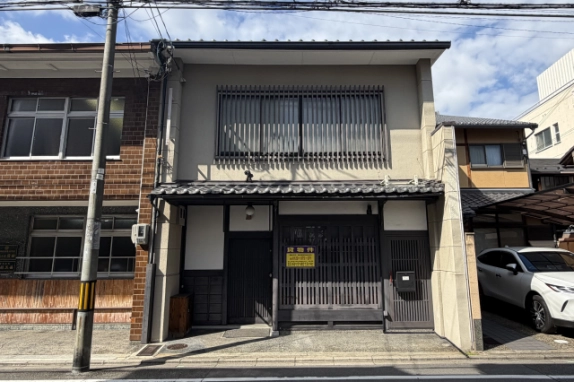 上京区石薬師町の京町家テナントを正面から見た外観。2階に縦格子の窓があり、1階には瓦の庇の下に格子戸と左手の玄関扉が並ぶ