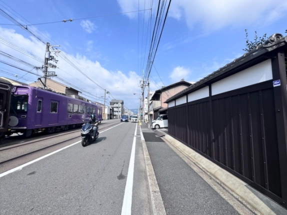 京町家の黒い板塀に沿う三条通。左手の線路を走る嵐電の車両