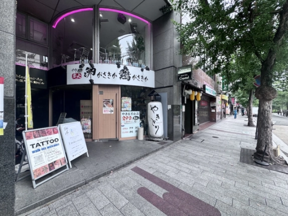 京都市中京区材木町・木屋町不動ビルの入口付近。1階店舗の看板と街路樹のある歩道