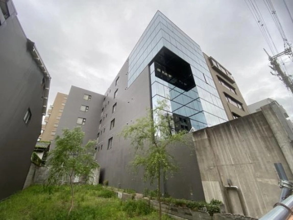 ストークビル三条烏丸を側面から見上げた外観。ガラス面の大きなくぼみと手前の植栽