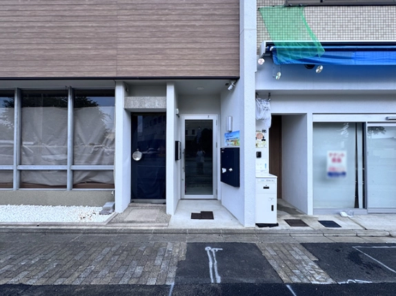 西工務店ビルの地上階入口正面。横に並ぶ濃色の扉とガラス扉