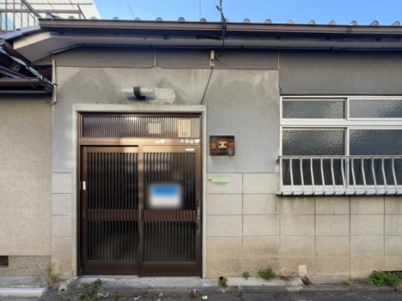 正面から見た玄関。格子の欄間がある茶色の引き戸と上部の照明、右に型ガラスの窓と白い面格子