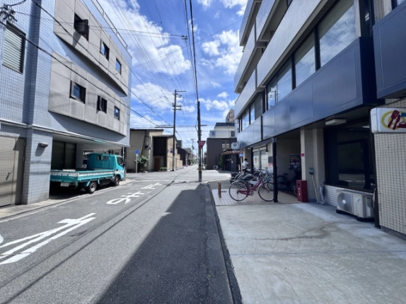 三輝ビルを右手に見た前面道路。建物脇の駐輪スペースと向かい側の建物