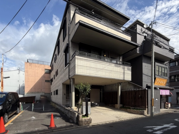 左斜め前から見た外観。小窓が並ぶ側面の外壁と2階の張り出したバルコニー、左隣に駐車場
