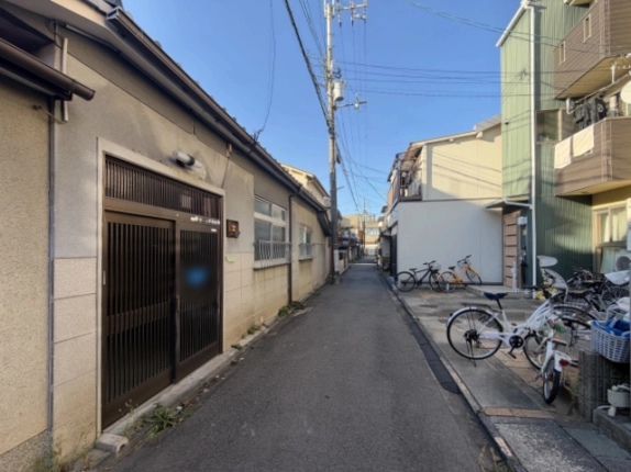 下京区の路地から見た外観。左手に格子戸の玄関と窓、右手の向かいには自転車が並ぶ建物
