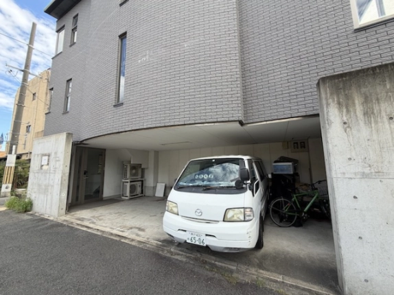 1階の駐車スペースと入口まわり。奥の室外機と停車中の車、右手の自転車