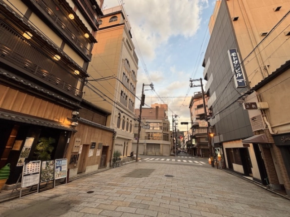 GION GLASS周辺の石畳の通り。左手のビルと周辺店舗、奥の交差点