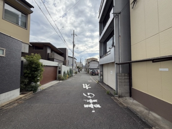 右京区西院の建物前の道路を見通した様子。右側にタイル張りの建物と1階のシャッター、左側に住宅が並ぶ