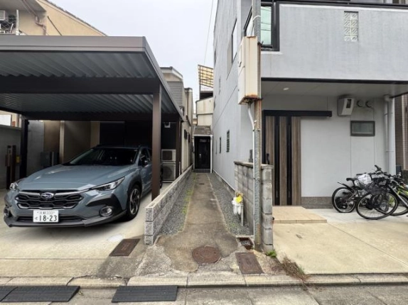 前面道路から見た一棟貸店舗事務所への入口。左のカーポートと右の住宅の間を、奥の黒い玄関まで細い通路が続く