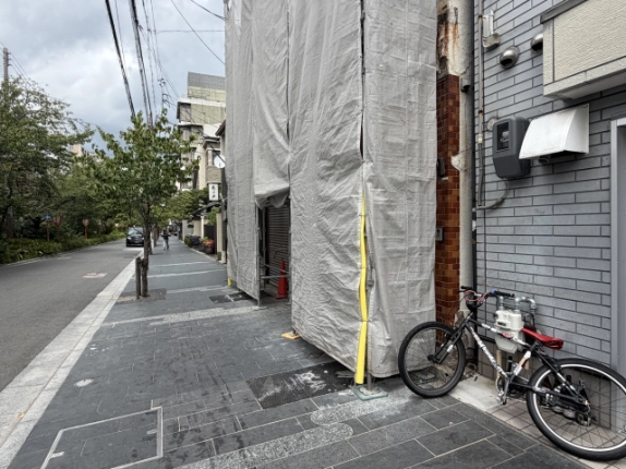 木屋町松原の1階貸店舗を斜めから見た様子。工事中の建物前に続く石張りの歩道と街路樹