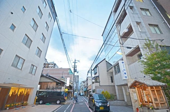 THE GATE Karasumaを右手に見た前面道路。建物脇の小さな祠と周辺の街並み