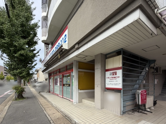 西京区のイチョウ並木の歩道から斜めに見た建物。赤いサッシのガラス面と黄色いブラインド窓が並ぶ1階、右奥に鉄骨の外階段