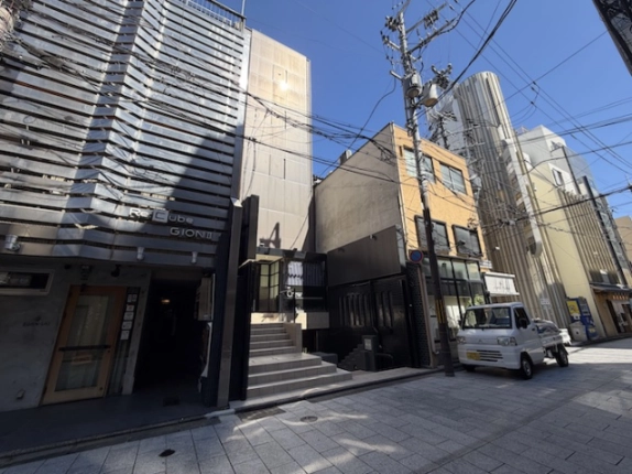 祇園四条駅から徒歩7分の通りに面したビルを斜めから見た外観。左隣は横縞模様の外装のビルで、通りの奥に高い建物が並ぶ