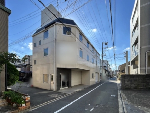 二条城前駅徒歩7分の貸事務所ビルを左斜め前から見た全景。紺色の屋根と屋上の塔屋、側面の窓と白い扉、黒タイルの入口が見える