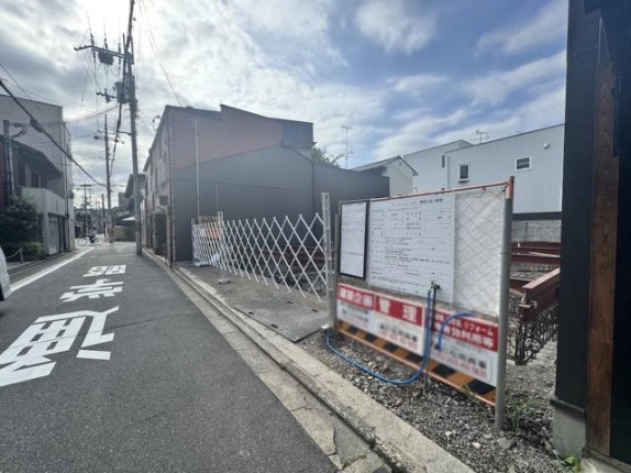 建設現場前を反対方向に見た様子。右手に工事案内板と仮囲い、奥へ続く前面道路
