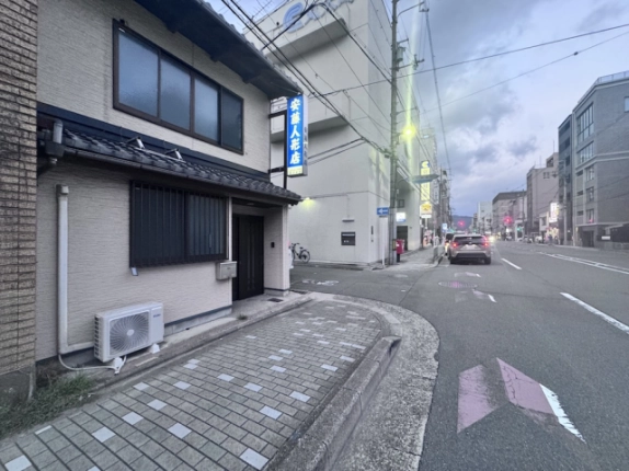 京町家の格子窓と玄関を左手に見た前面道路。曲線を描く歩道の縁と沿道の街並み