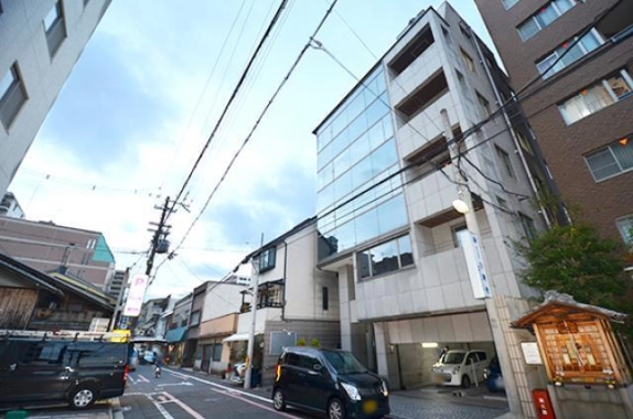五条駅近くの貸事務所が入るビルを反対側から見た外観。ガラス面と地上階の駐車スペース