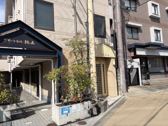 コーポ鍋島の入口まわりを斜めから見た様子。クリーム色の壁と隣接する植栽