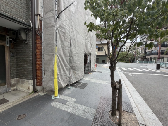 木屋町松原店舗前を反対方向に見た道路。左手に工事中の建物、右手に街路樹、奥に横断歩道