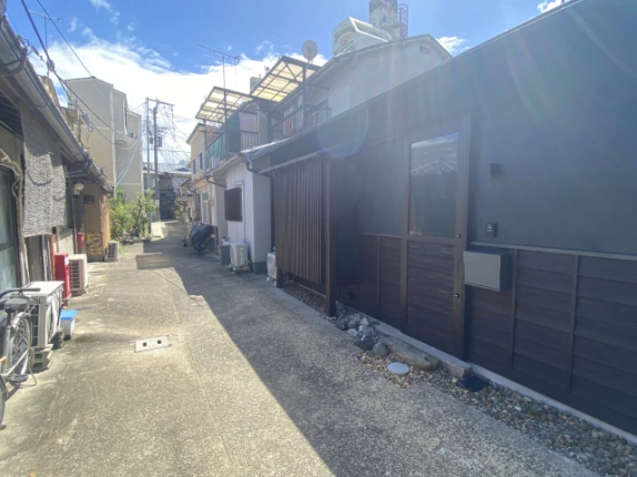 西陣の杜を右手に見た路地。建物の板張りの腰壁と周辺の住宅