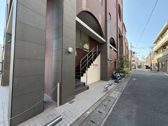 桂駅徒歩1分の2階貸店舗へ続く外階段。灰色の柱とタイル敷きの歩道を斜めから見た様子