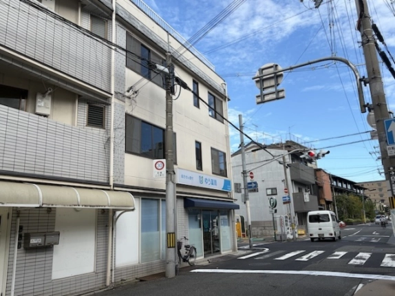 隣の建物側から斜めに見たビルの外壁と窓。右手には横断歩道のある交差点と車道が続く