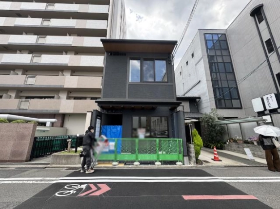 京都市中京区鯉山町・さきぞう室町会館の正面外観。2階の大きな窓と濃い灰色の外壁、撮影時の仮設フェンス