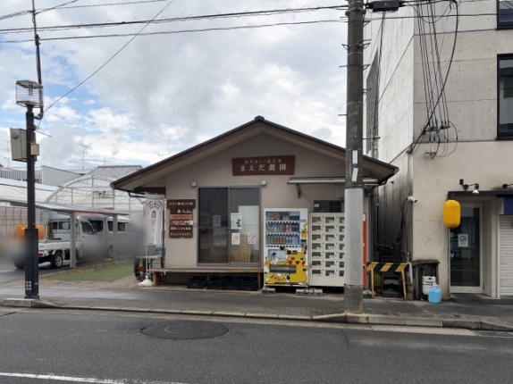 前面道路から見た切妻屋根の建物正面。「京やさい・近江米 まえだ農園」の看板と、飲料の自動販売機やロッカー式の販売機